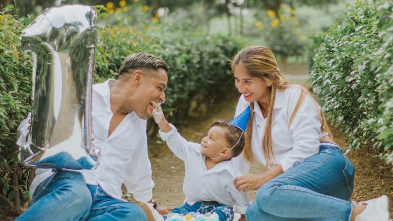 A joyful family celebrating their child's first birthday outdoors with cake and balloons.