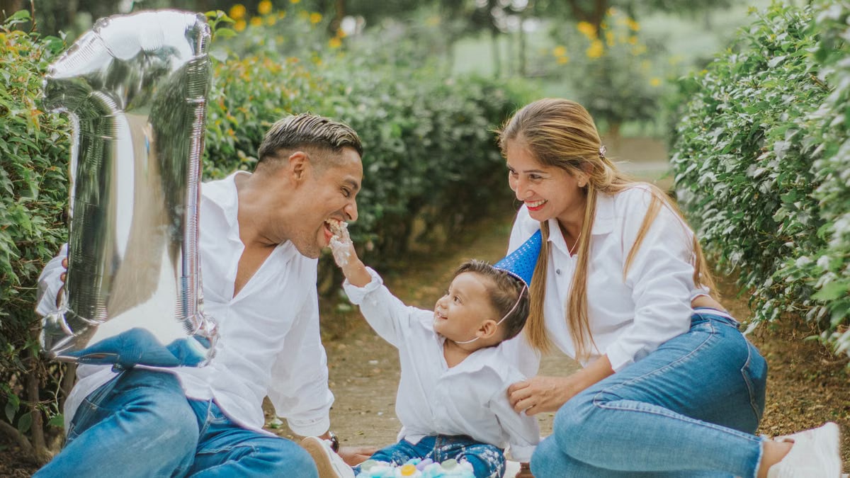A joyful family celebrating their child's first birthday outdoors with cake and balloons.