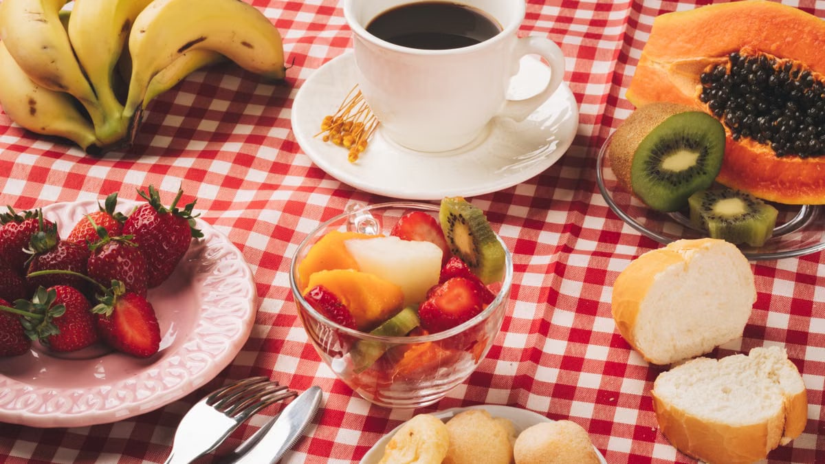 Delicious breakfast table with coffee, fresh fruits, and bread on a checkered tablecloth.